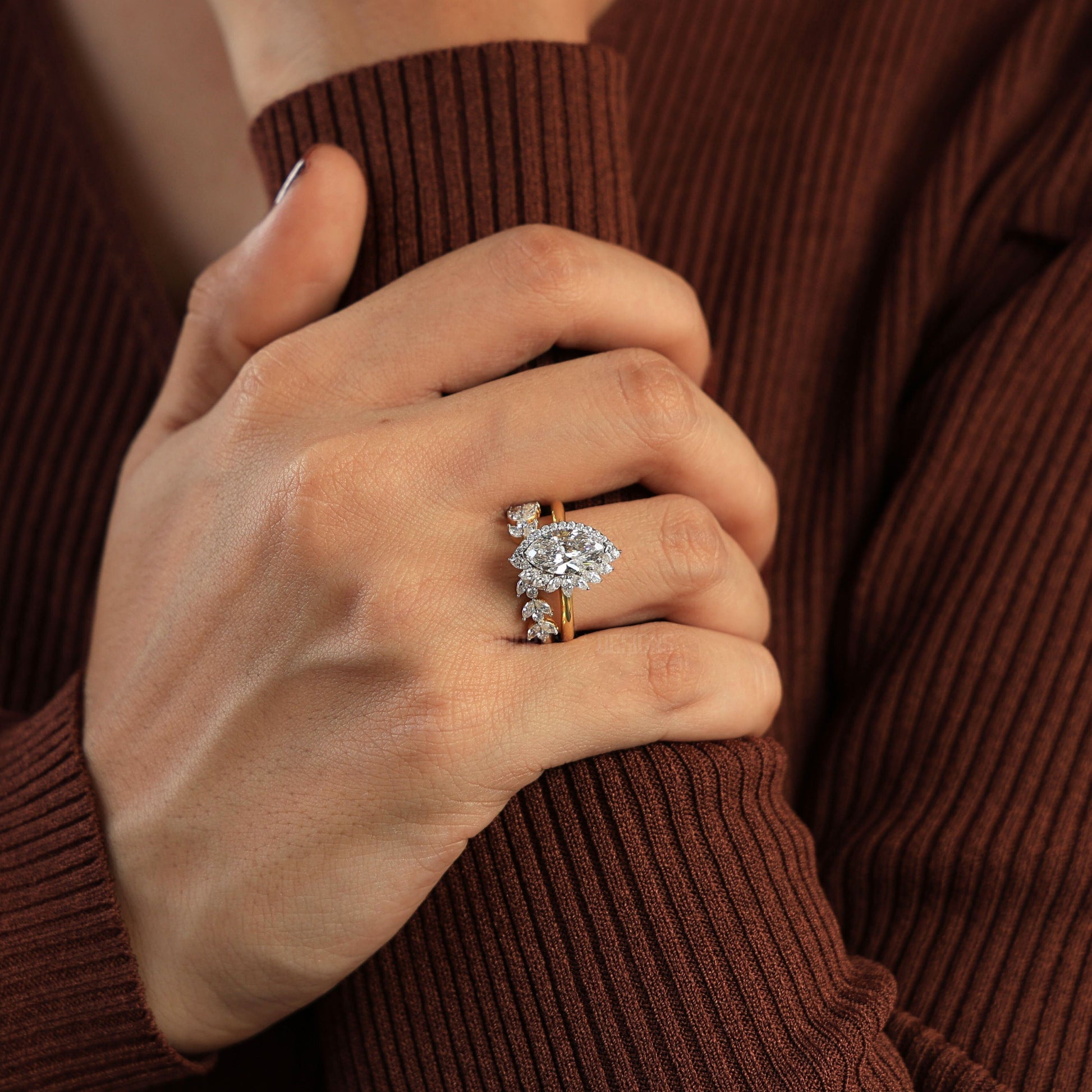 Hand wearing a diamond ring with a brown ribbed sweater background